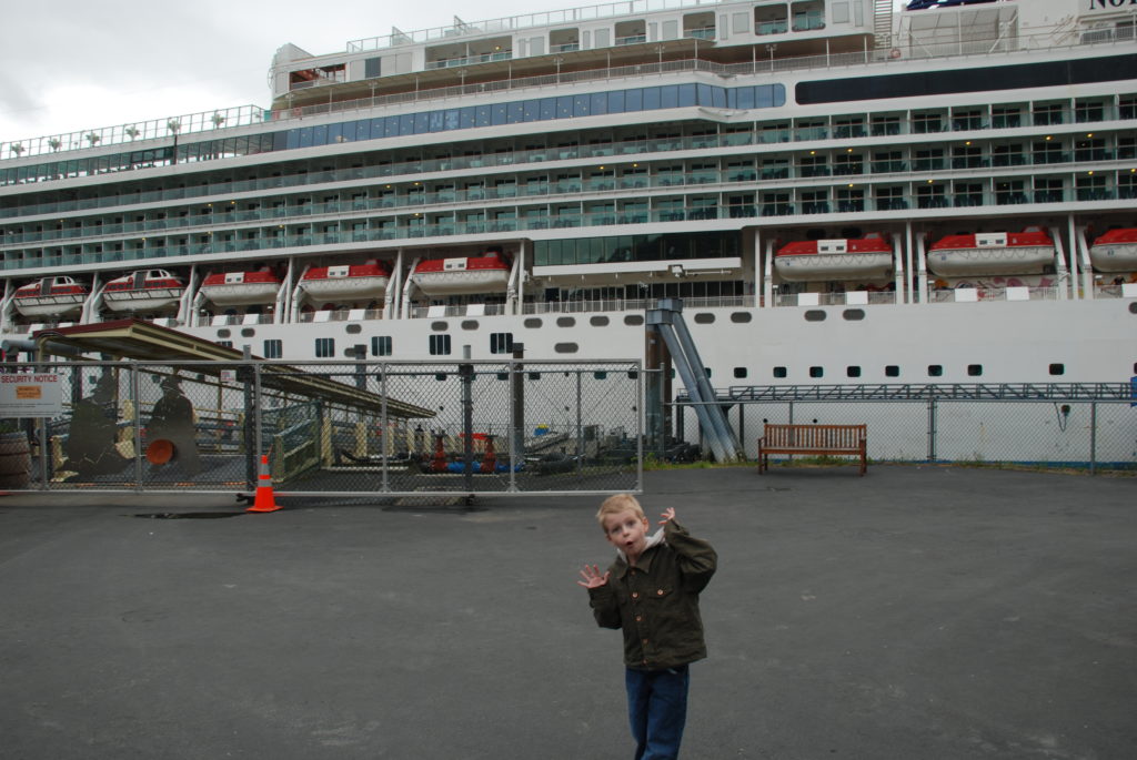 a boy standing in front of a large cruise ship