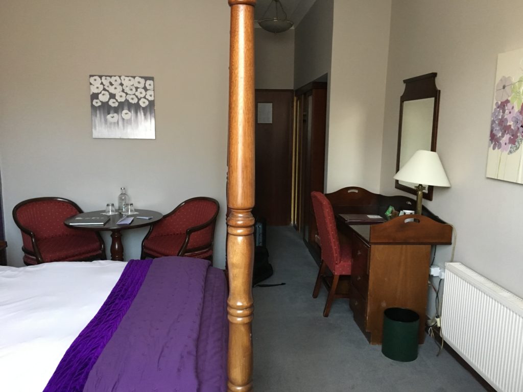 a bed with purple blanket and a table and chairs in a room