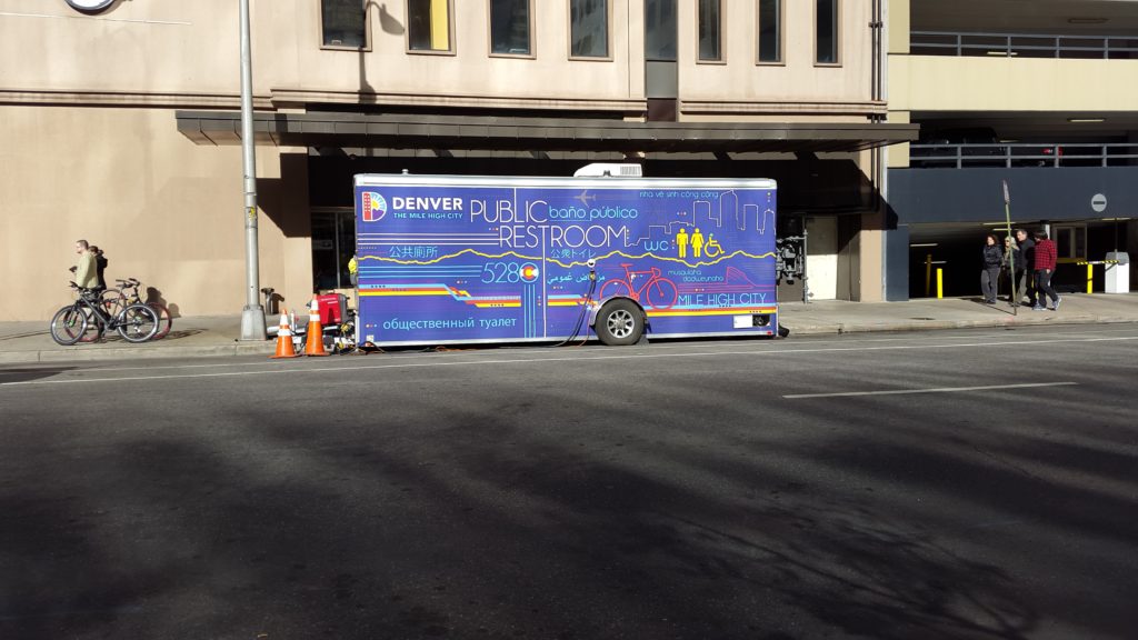 a blue and purple public restroom truck parked on the side of a road