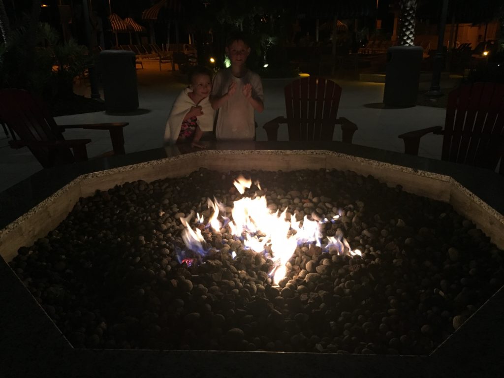 a couple of kids standing in front of a fire pit