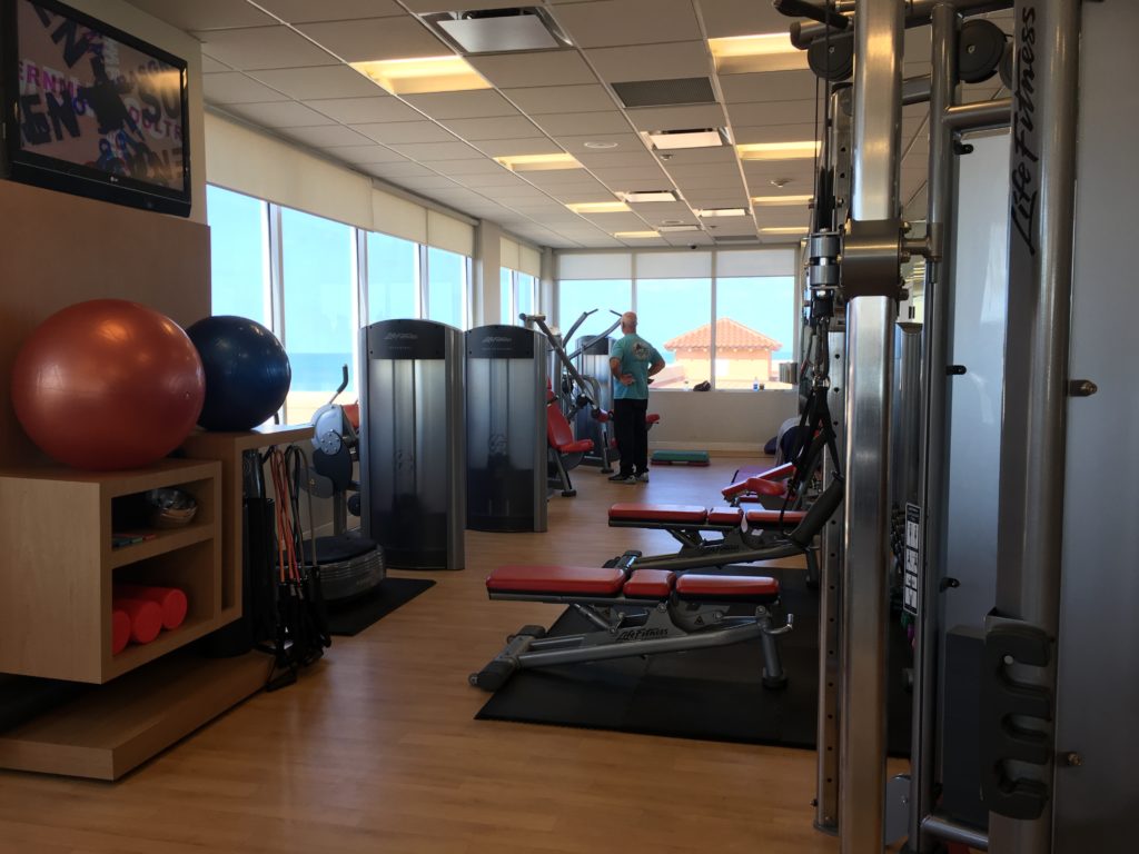 a room with exercise equipment and a man standing in front of the window