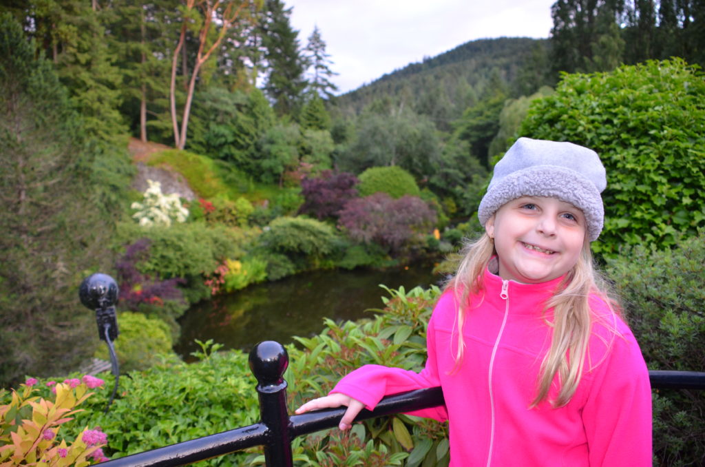 a girl in a pink jacket and hat leaning on a railing in front of a river