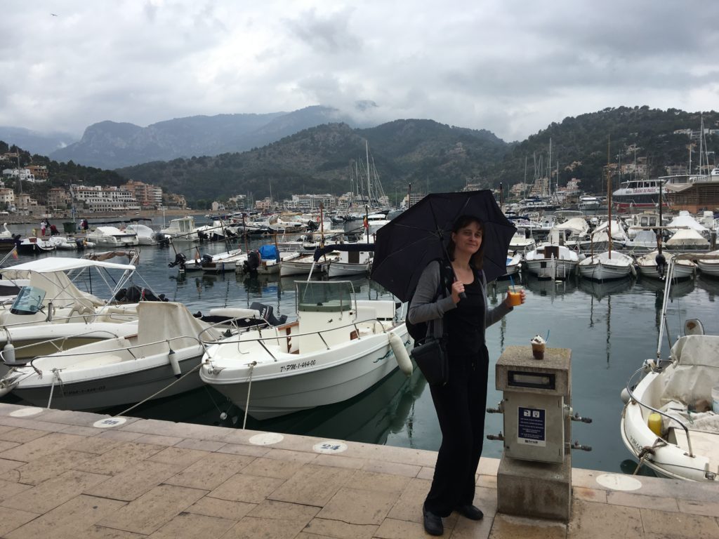 a woman standing on a dock with a black umbrella and a body of water with boats in the background