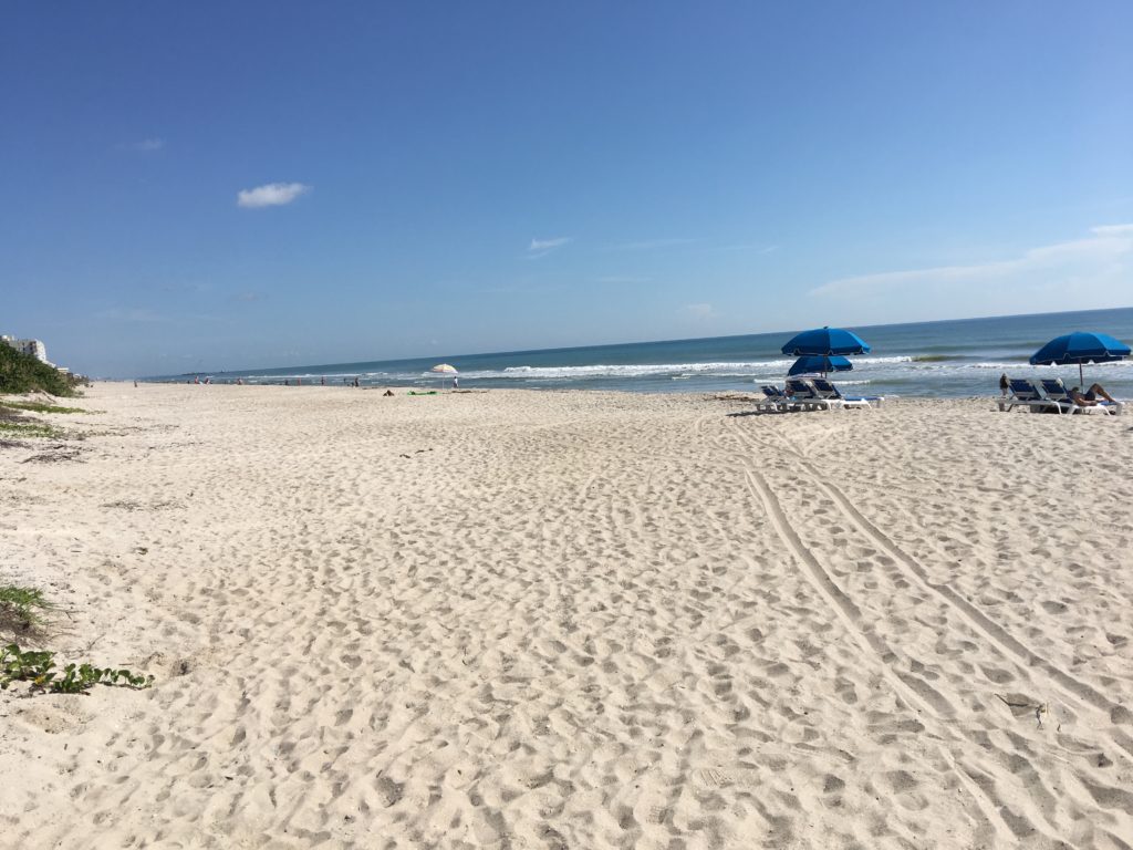 a beach with a blue umbrella and chairs