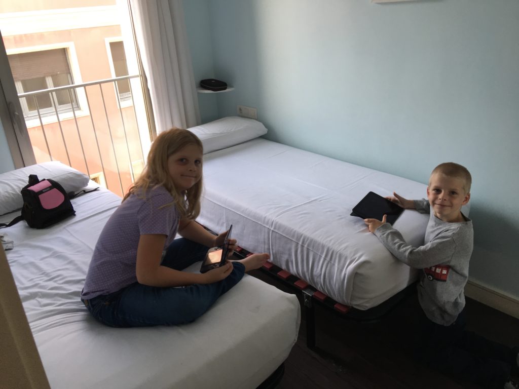 a boy and girl sitting on a bed with a tablet