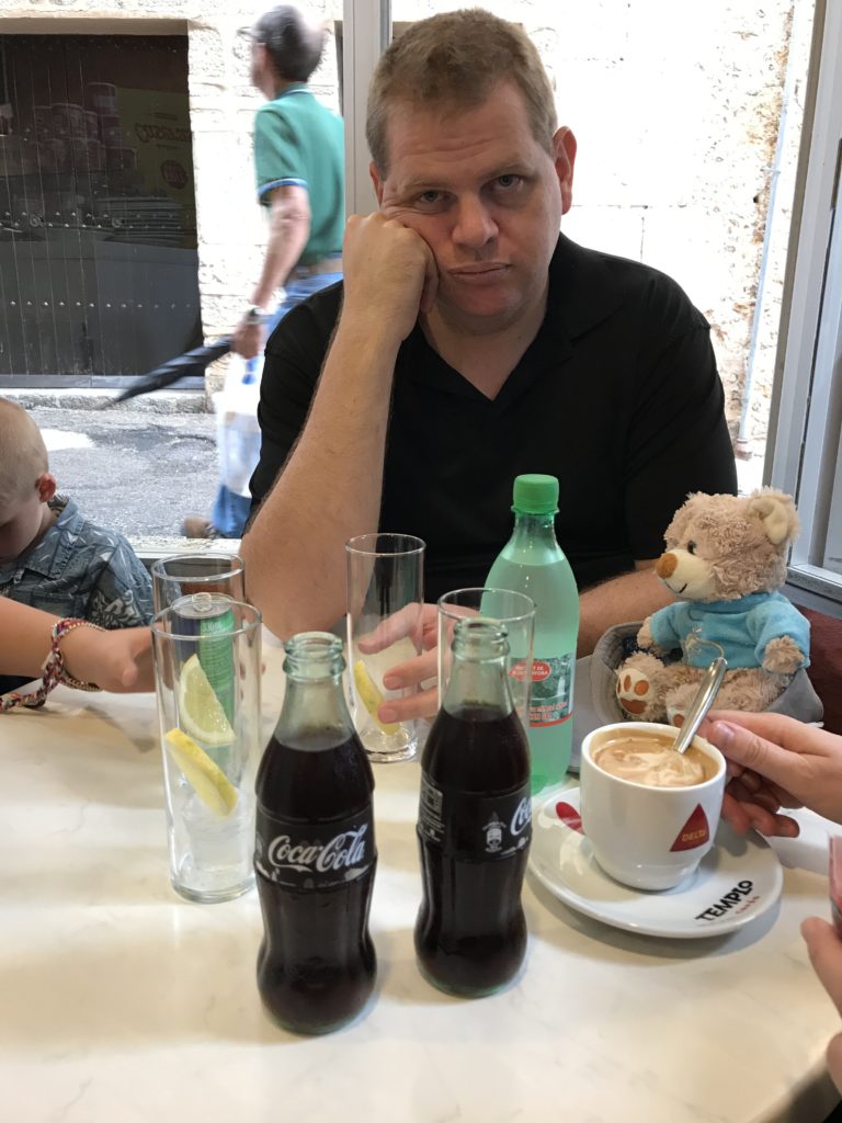 a man sitting at a table with drinks and a stuffed animal