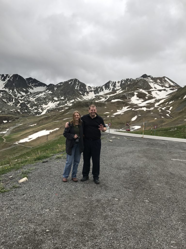 a man and woman standing on a road with snow covered mountains in the background