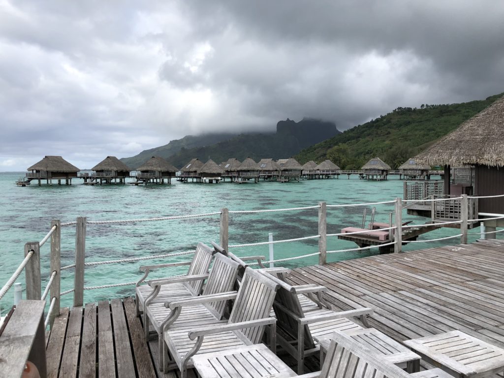 a wooden deck with chairs and a dock with huts on water