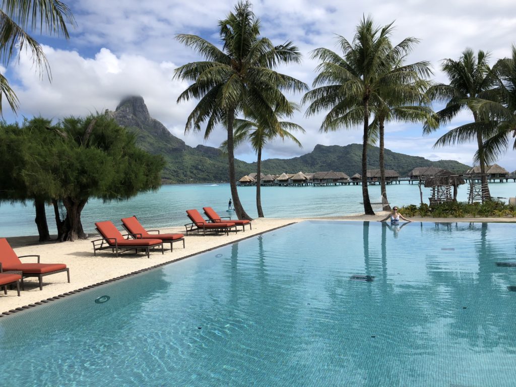 a pool with chairs and palm trees on the beach