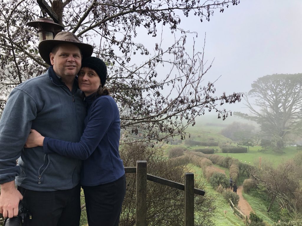 a man and woman standing on a railing with trees and a path
