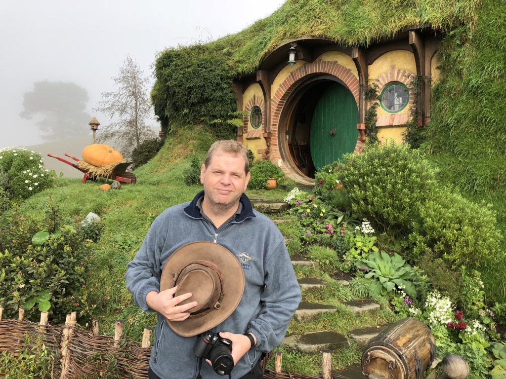 a man holding a hat in front of a green house