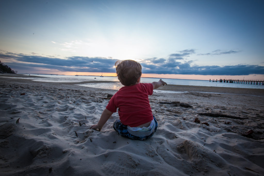 a baby sitting on sand at the beach