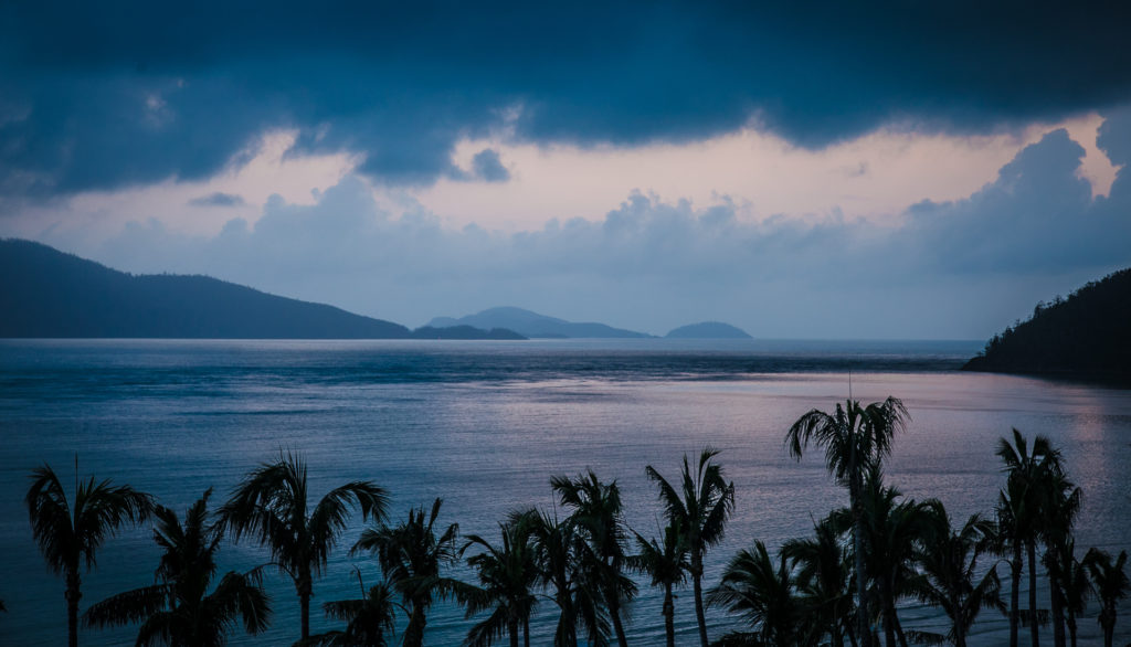 a body of water with palm trees and islands in the background