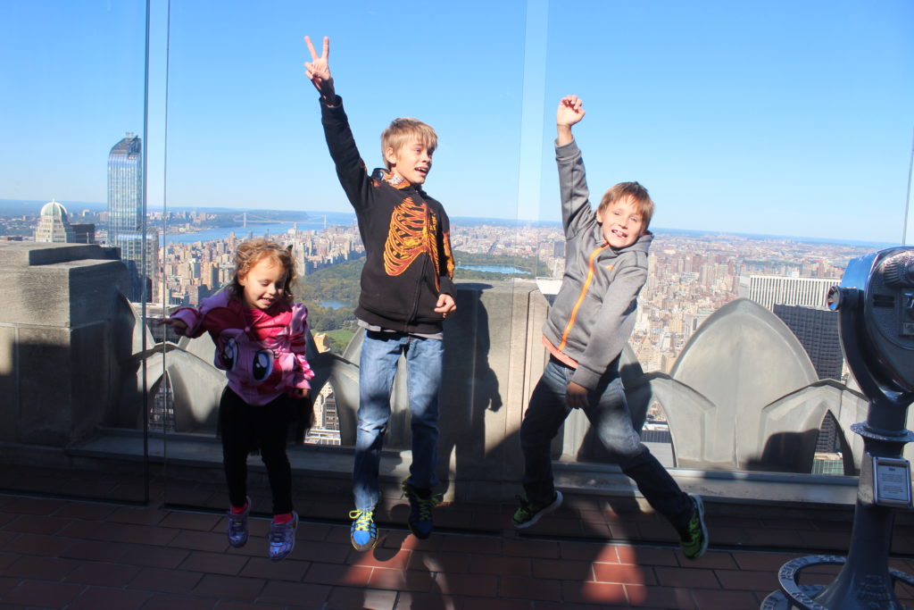 a group of kids jumping on a ledge with a city in the background