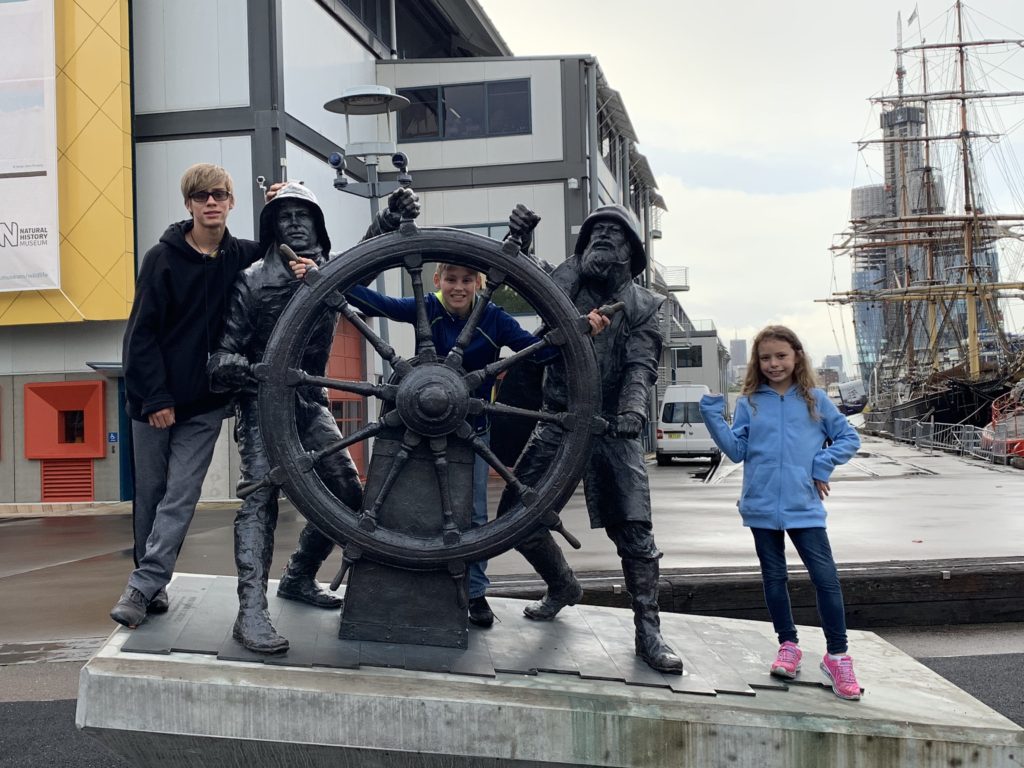a group of people standing next to a statue of a ship steering wheel
