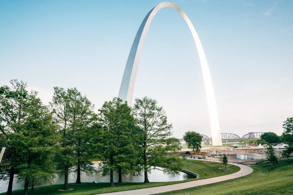 a large arch with trees around it with Gateway Arch in the background