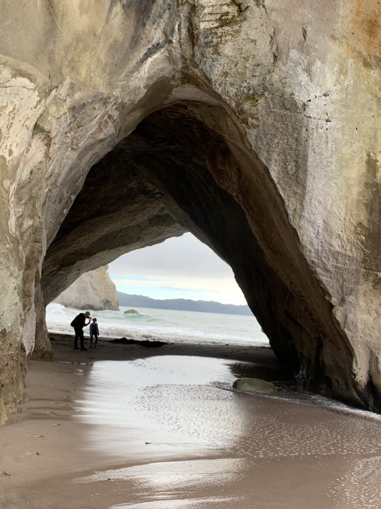people standing on a beach with a cave in the background