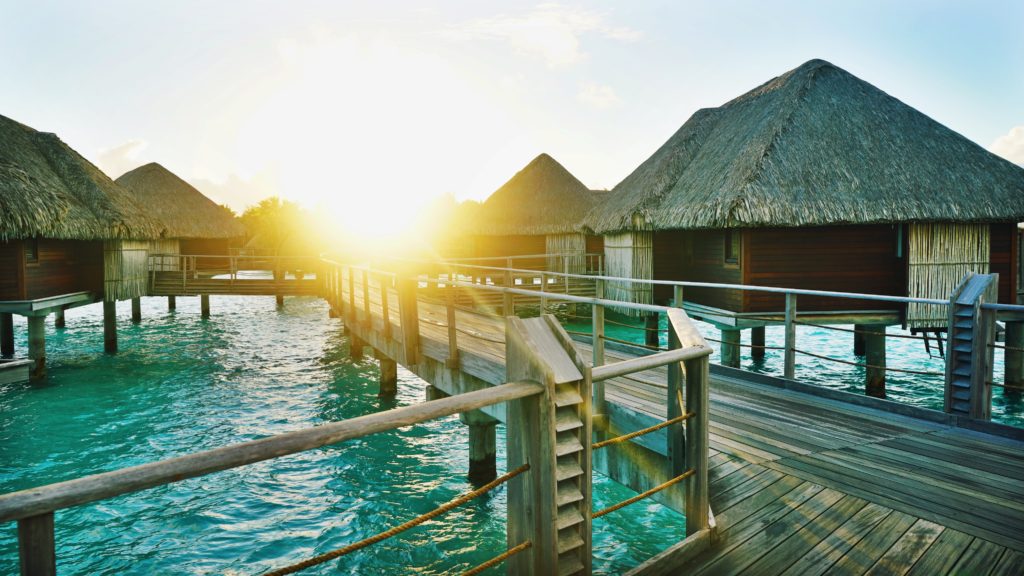 a wooden walkway over water with huts and a thatched roof