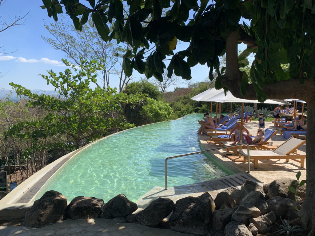a pool with people sitting on lounge chairs and umbrellas