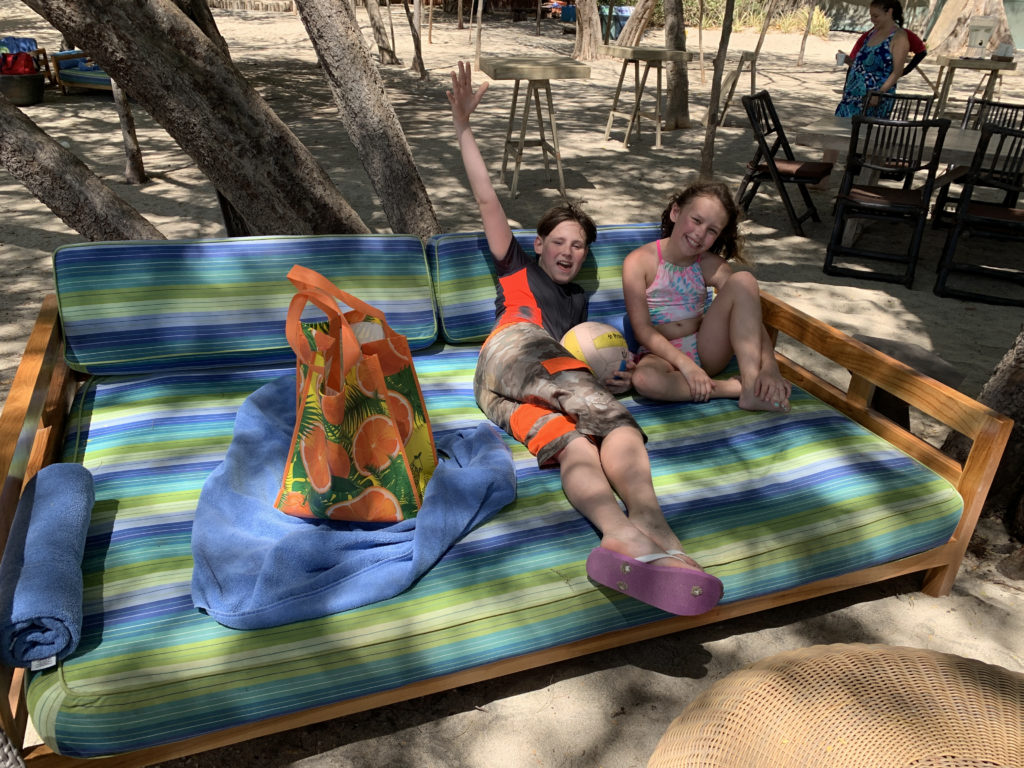 a two children sitting on a bed under trees