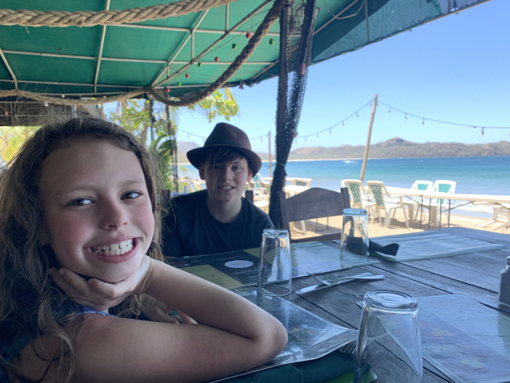 a boy and girl sitting at a table with water in the background