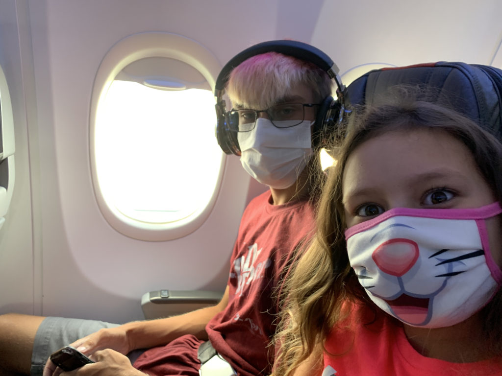 a boy and girl wearing face masks and sitting in an airplane