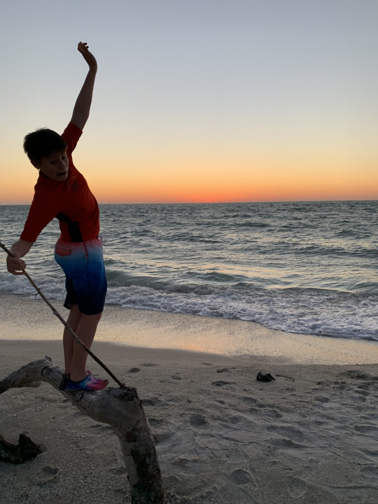 a boy standing on a log on a beach