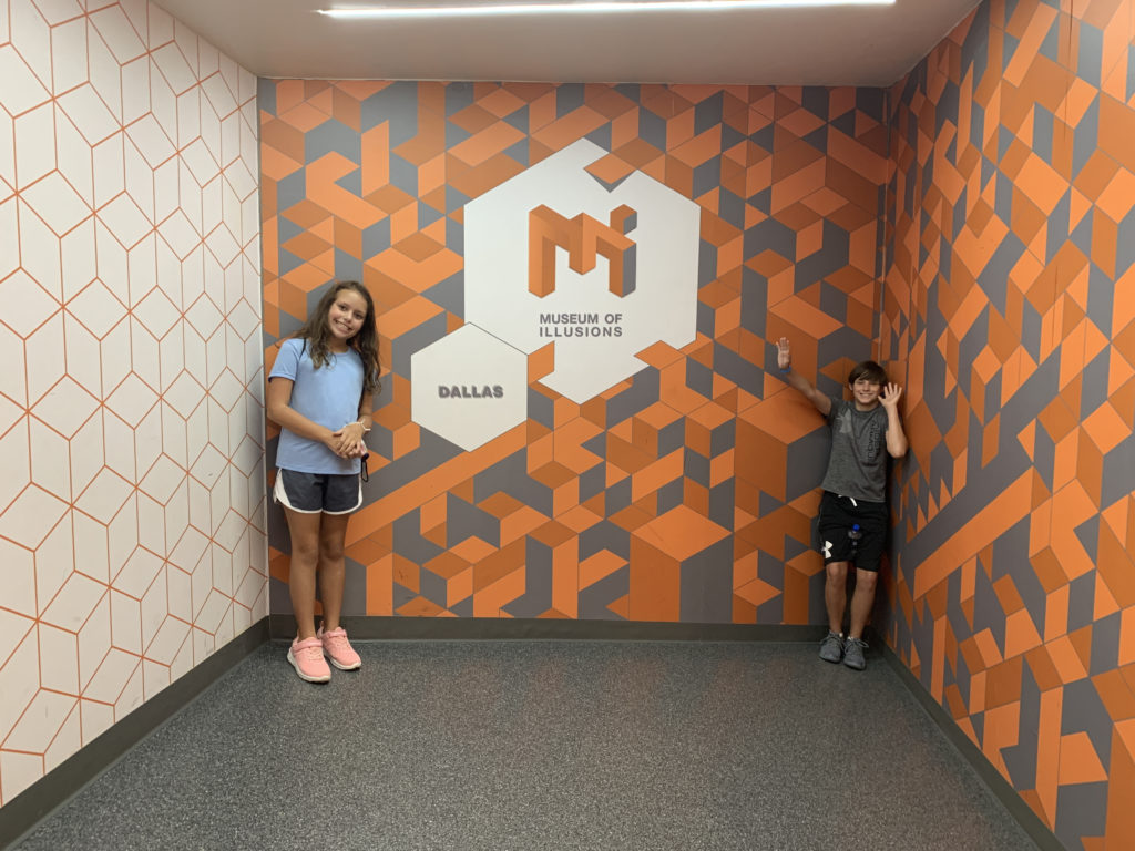 a boy and girl standing in a room with a wall with a logo