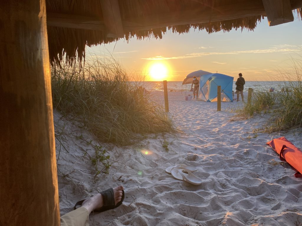 a person's feet on a beach with a tent and grass