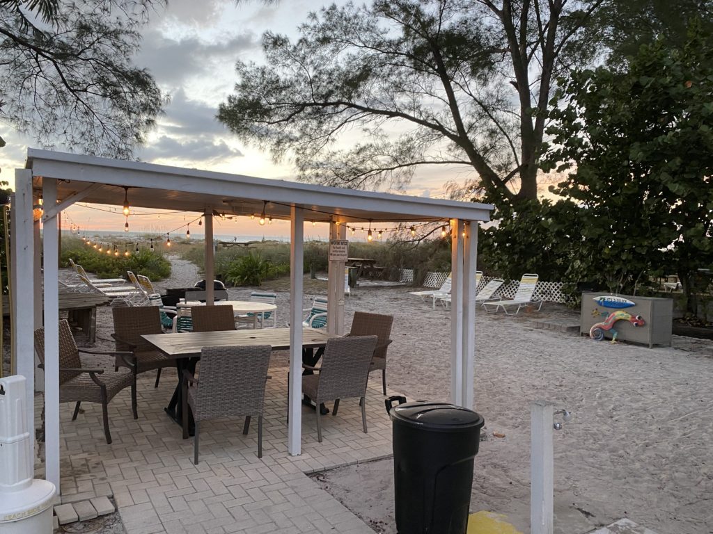 a patio with chairs and tables on a sandy beach