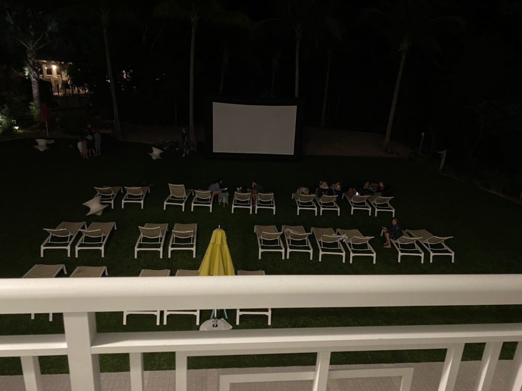 a group of people sitting in a lawn with chairs and a screen