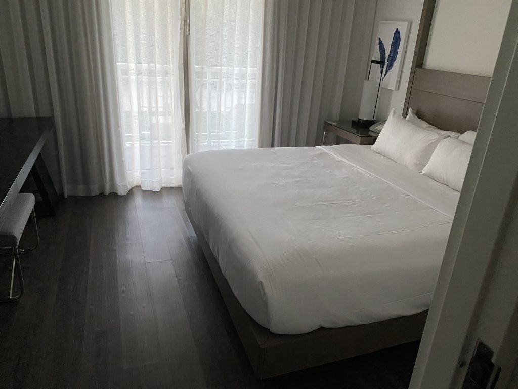 a bed with white sheets and pillows in a room with white curtains