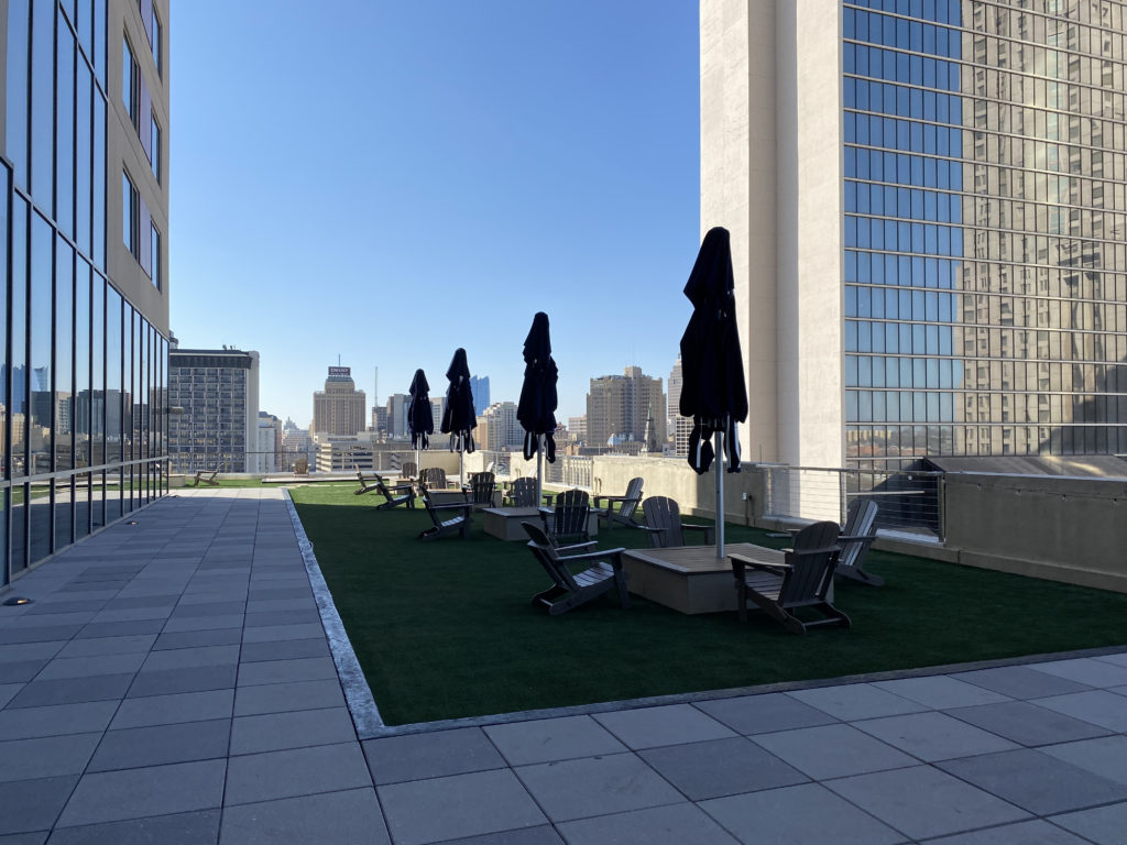 a patio with chairs and umbrellas on grass and a city skyline