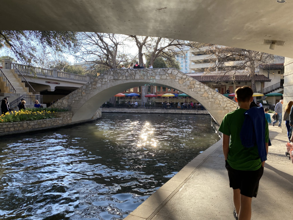 a man walking on a path under a bridge over a river