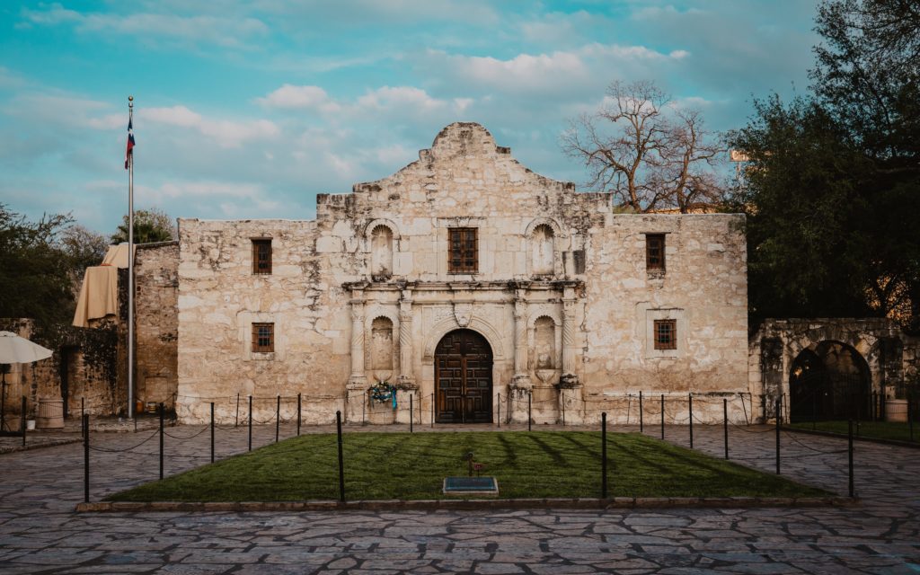 a stone building with a stone fenced courtyard with Alamo Mission in San Antonio in the background