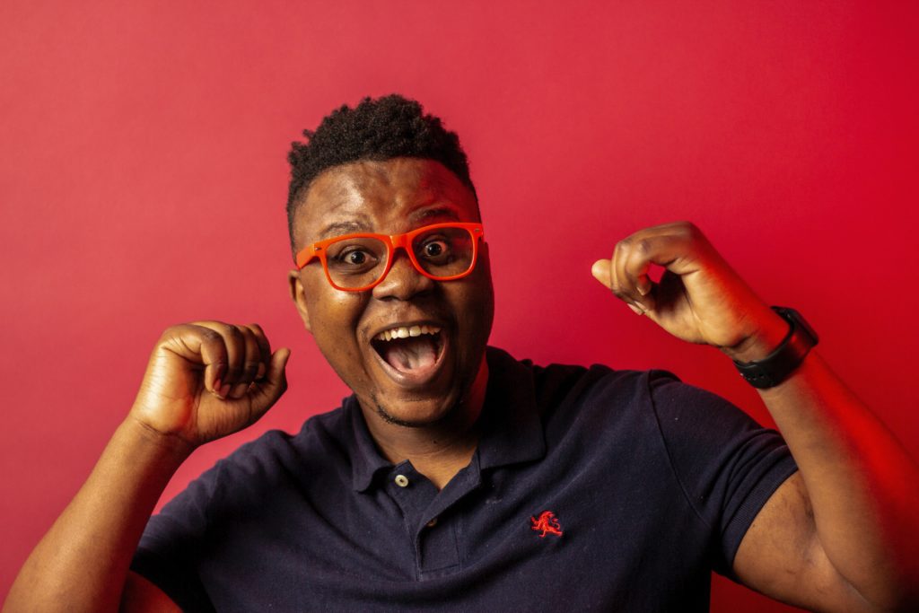 a man with orange glasses and blue shirt with his mouth open