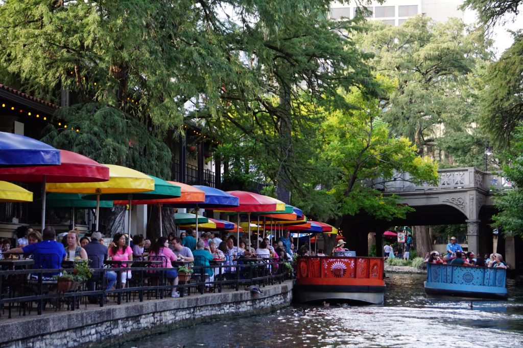 a group of people sitting at tables with umbrellas on the side of a river