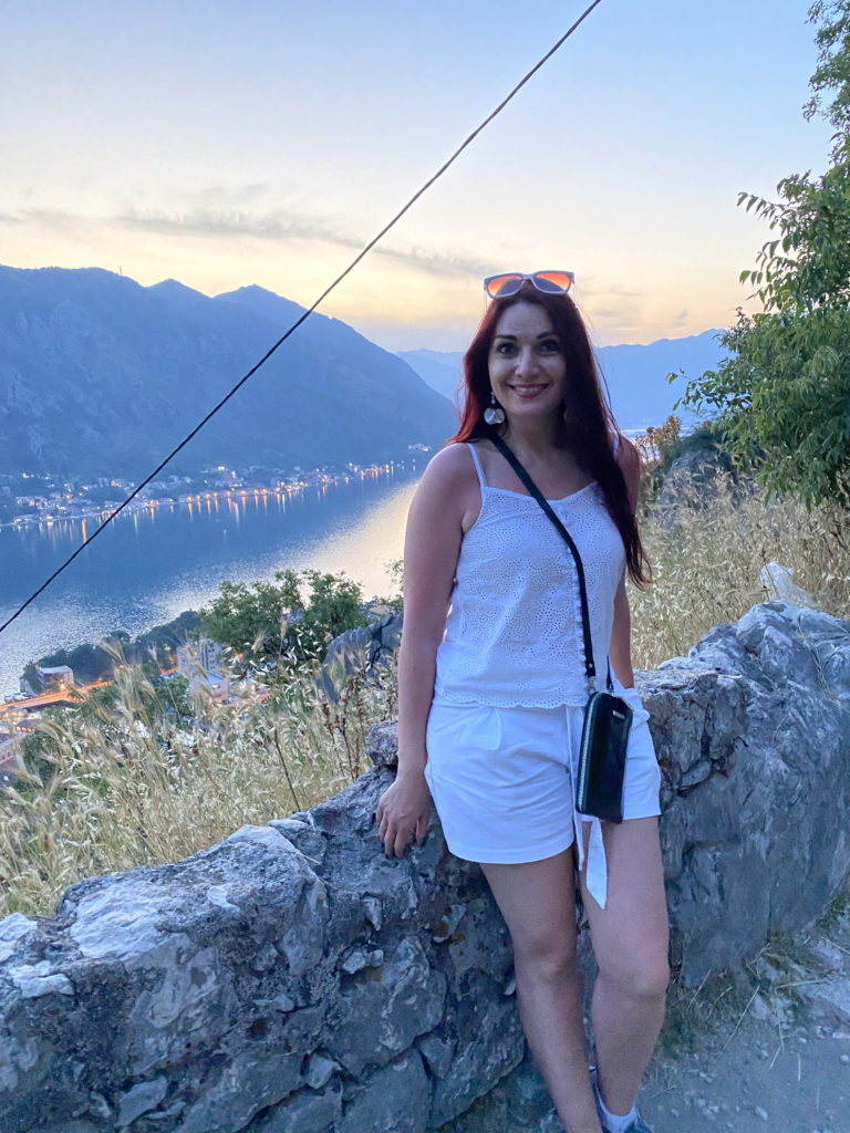 a woman standing on a rock wall with a body of water in the background