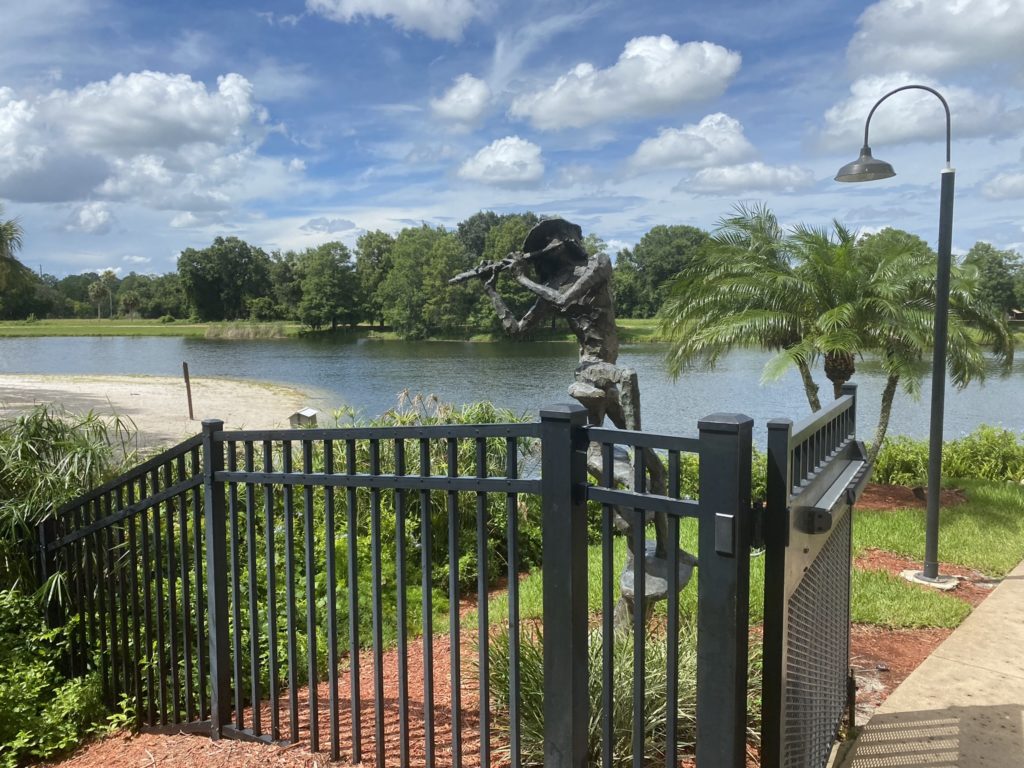 a statue of a man playing a flute on a fence by a body of water