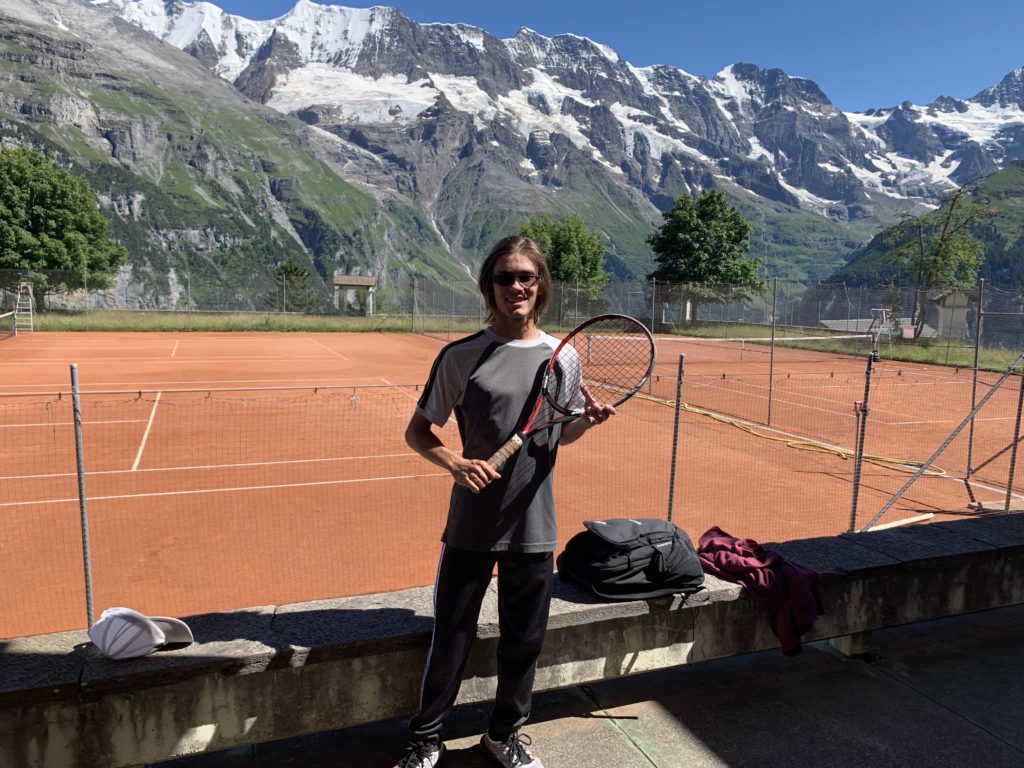 a person holding a tennis racket on a bench in front of a tennis court