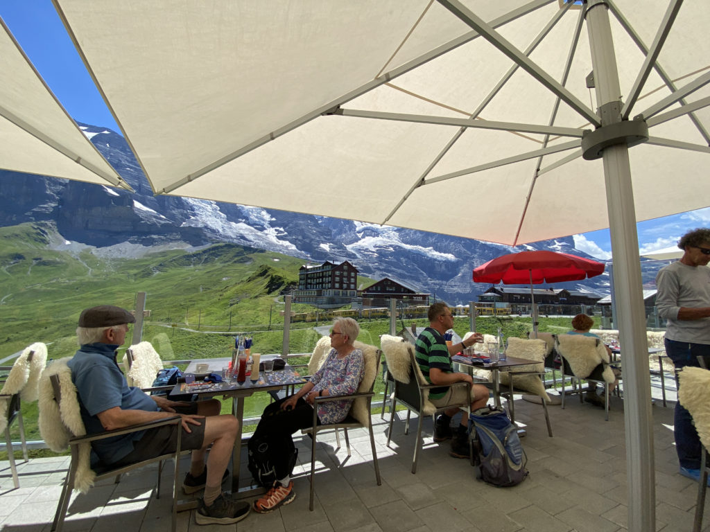 a group of people sitting at tables outside under umbrellas