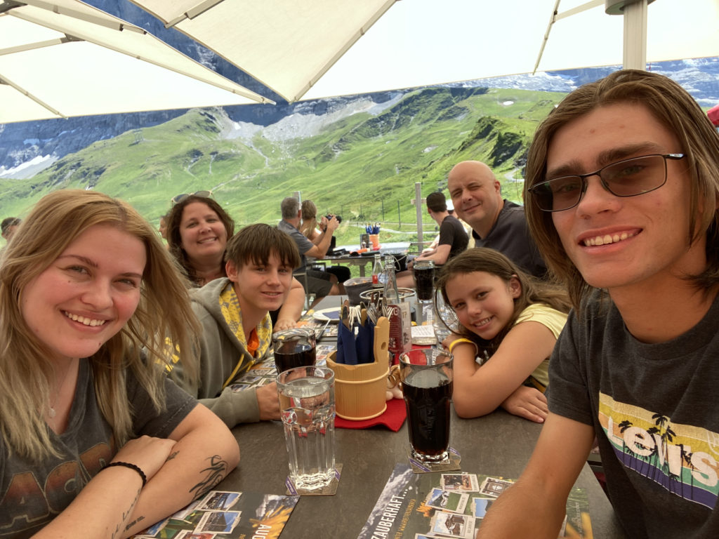 a group of people sitting at a table with drinks and mountains in the background