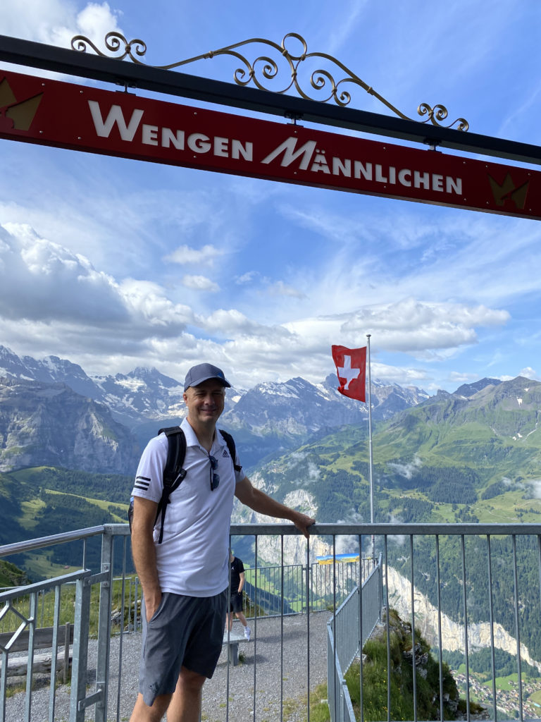 a man standing on a railing with a sign and mountains in the background