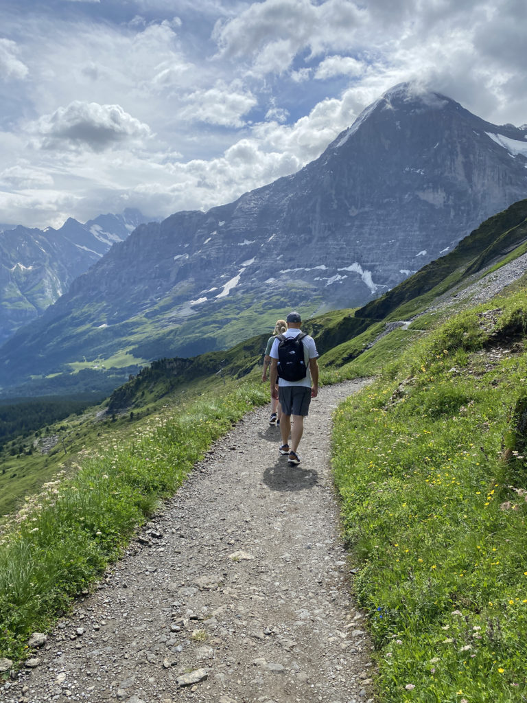 a man and woman walking on a path with mountains in the background