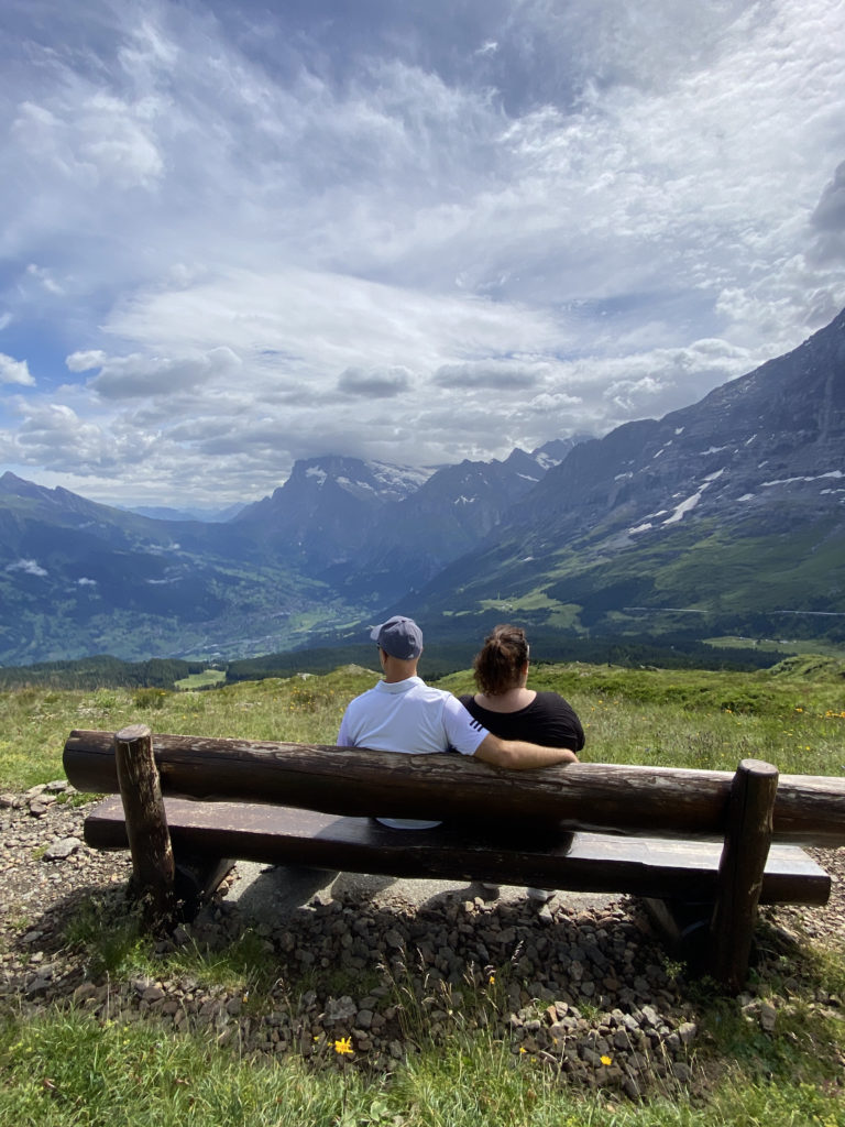 a man and woman sitting on a bench overlooking mountains