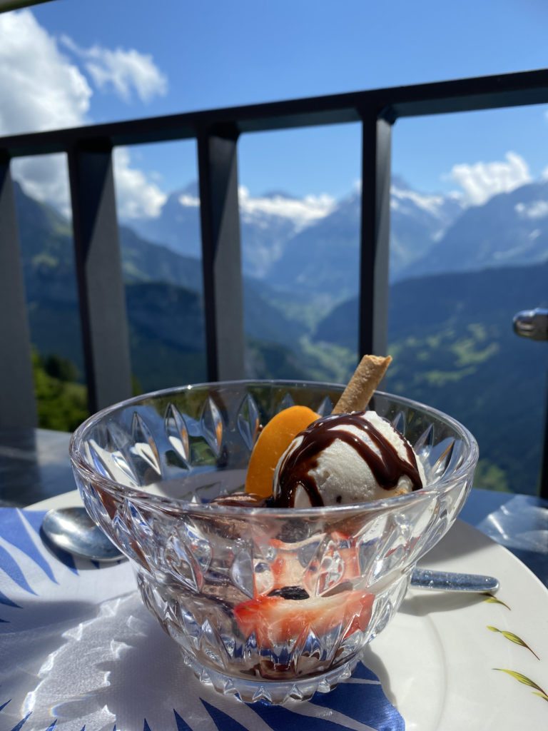 a glass bowl with ice cream and fruit on a table with a railing