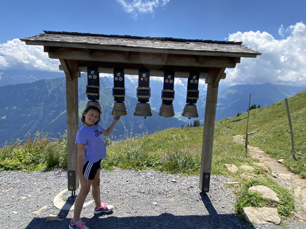 a girl holding a bell under a wooden structure