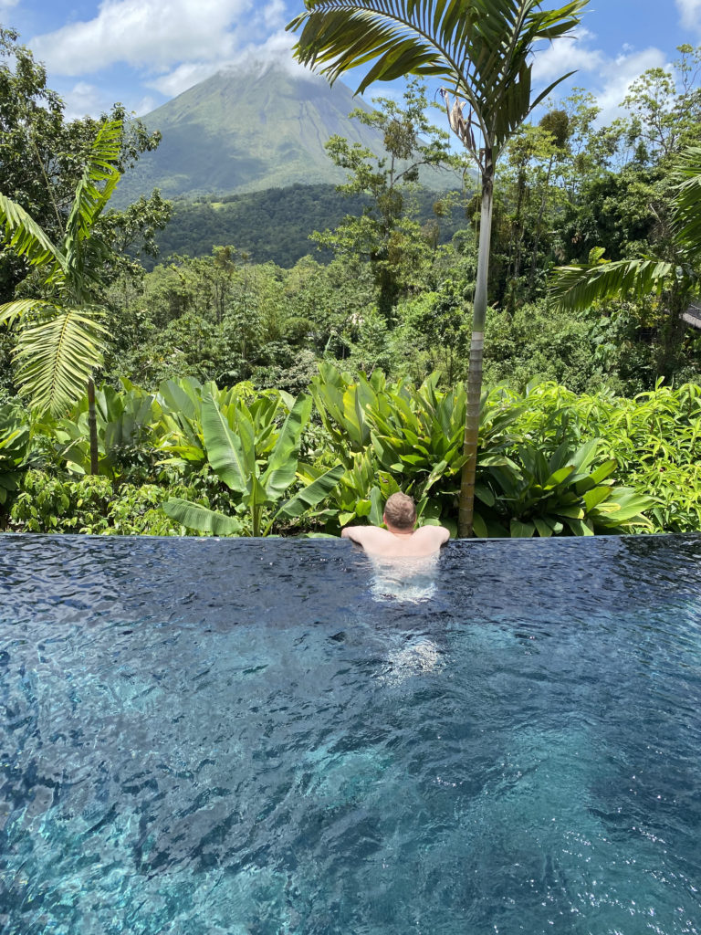a man in a pool with trees and mountains in the background