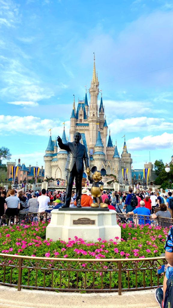 a statue of a man and mouse in front of a castle with Magic Kingdom in the background