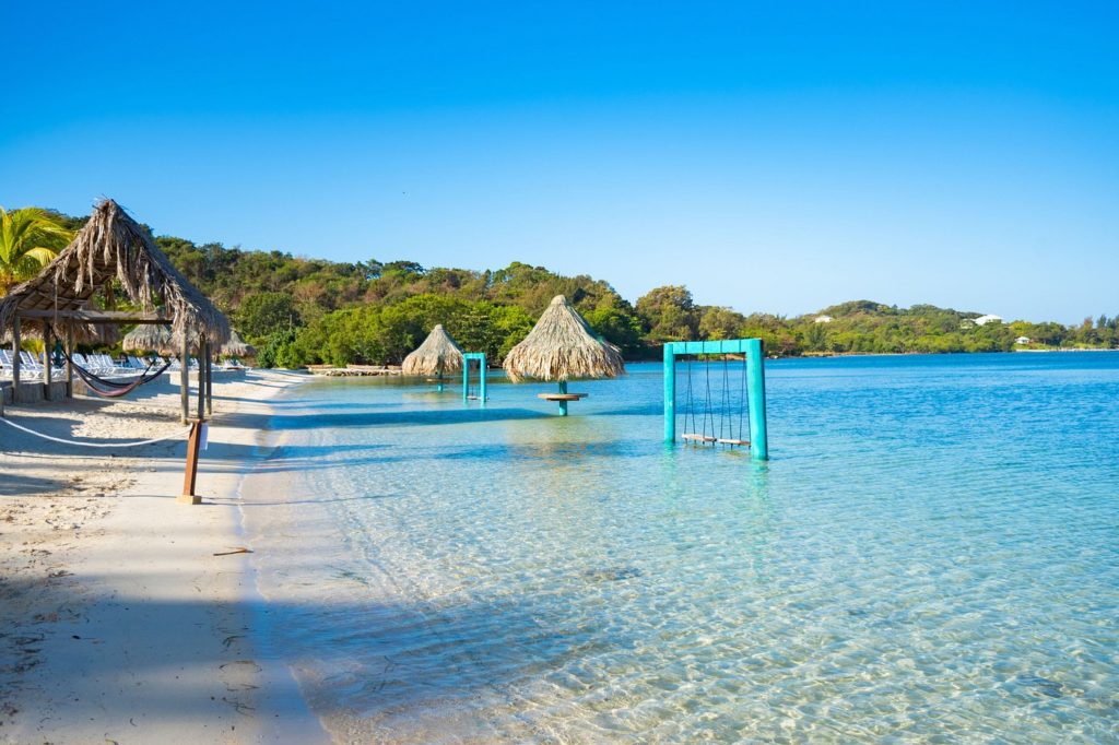 a beach with a swing and thatched umbrellas